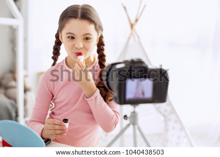 Beautiful lips. Adorable pre-teen girl with two braids applying lipstick and smiling during filming a makeup tutorial