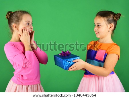 Girls with shocked faces pose with presents on green background. Children open gifts for Christmas. Birthday surprise concept. Sisters with wrapped gift boxes share presents for holiday.