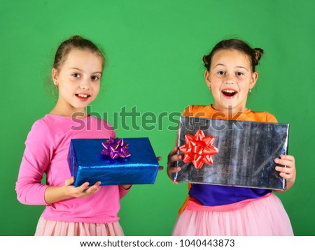 Sisters with wrapped gift boxes for holiday. Children with happy faces pose with presents on green background. Girls open gifts for Christmas. Xmas holidays concept.