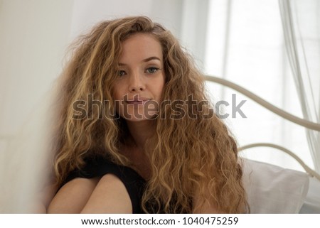 Blond woman sitting on a white bed leisure activities.
