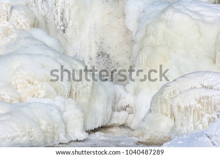 Snow and ice on the banks of the river near the waterfall on a sunny day