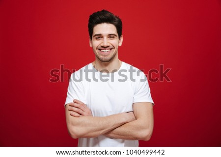 Portrait of a smiling young man in white t-shirt standing with arms folded isolated over red background