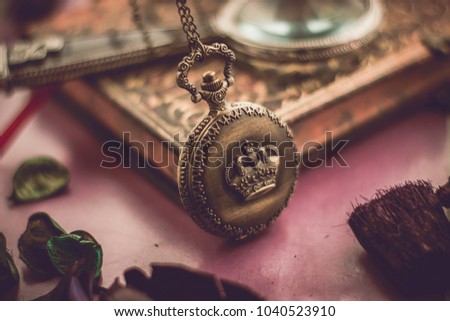 An old pocket watch on an old book. Pink flower and a magnifying glass. Golden with pink tone