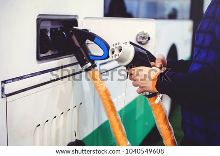 Details of electric vehicle charging city bus transport. Green and renewable energy sources. man holds in his hand. Royalty-Free Stock Photo #1040549608