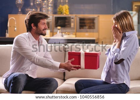 A man gives his own gift to his boyfriend as a sign of love for their anniversary. The girl is happy with the surprise she has just received. Concept of: gift, love, valentine's day, anniversary.