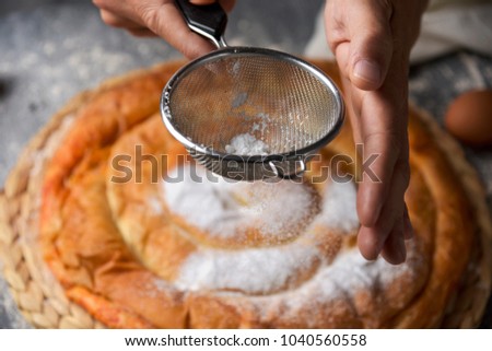 closeup of a young caucasian man sprinkling powdered sugar on an ensaimada, a pastry typical of Mallorca, Spain, placed on a rustic wooden table