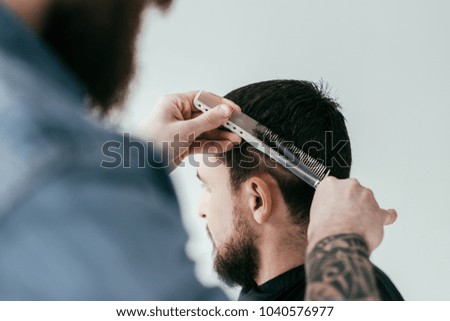 cropped image of barber cutting customer hair with scissors and comb at barbershop isolated on white