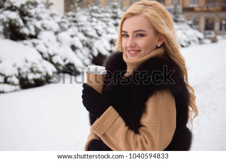 Portrait of european style fashionable woman drinking coffee in winter park.