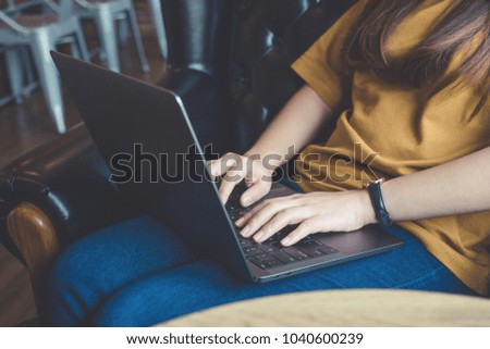 Closeup image of woman's hands working and typing on laptop keyboard while sitting on sofa