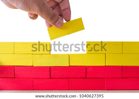 Concept of building success foundation, Hand on the last yellow puzzle wooden blocks in the shape of a wall isolated white background Royalty-Free Stock Photo #1040627395