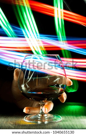 A glass of cognac in a woman hand on bright background with bokeh effect.