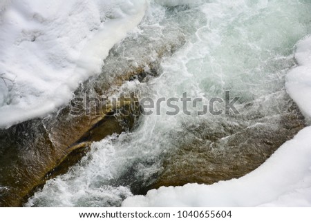 Frozen fast mountain river in winter. Spring melting of ice, springtime thaw.