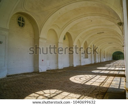 Classic vaulted archway leading along building with open side and sunlight casting repeating shadows through vaulted windows..