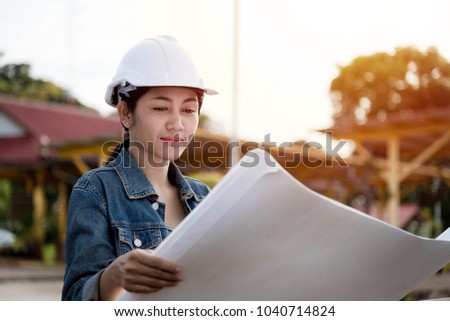 Beautiful Asian girls engineers wearing a jeans shirt reading blueprint design project concept at construction site.