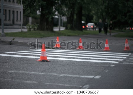 Macro shot of road traffic cones with orange and white stripes standing on street on gray asphalt during road construction works. Just painted white street lines on pedestrian crossing