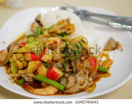 Close up of fresh appetizing stir-fried sea foods in sweet red curry paste with onion and Chinese long bean, on steamed rice - delicious and healthy Thai street food menu, a la carte