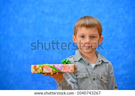 A boy with a gift in his hands in the studio on a blue background looks at the camera when shooting