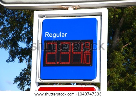 Red White and Blue Sign at Gas Station Indicating Regular $2.34 and 9/10 Price with Green Leaves in the Background in a Sunny Afternoon
