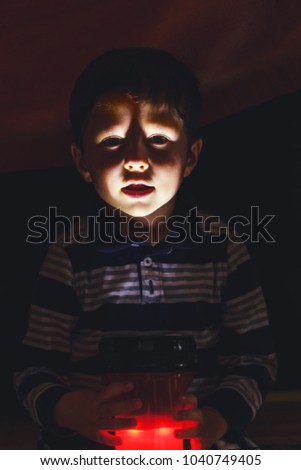 Boy with facial expressions of horror, fear and feelings of concern. Emotions of moderate panic, fright, horror and scare on the face of kid, lit with a flashlight in the dark background. 