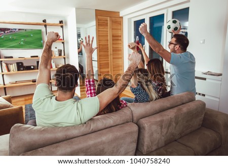 Happy friends or football fans watching soccer on tv and celebrating victory at home.Friendship, sports and entertainment concept. Royalty-Free Stock Photo #1040758240
