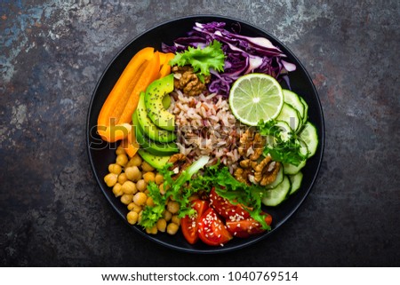 Buddha bowl dish with brown rice, avocado, pepper, tomato, cucumber, red cabbage, chickpea, fresh lettuce salad and walnuts. Healthy vegetarian eating, super food. Top view Royalty-Free Stock Photo #1040769514