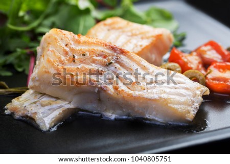 Cod fillets with olives and capers on black plate / Mediterranean cuisine