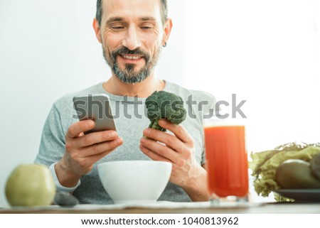 Best quality. Satisfied handsome unshaken man having breakfast in the bright room smiling and looking at a broccoli. Royalty-Free Stock Photo #1040813962