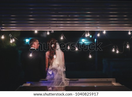 Enamored newlyweds gently embrace. Wedding ceremony in nature. The lights of the electric garland illuminate the wedding party.
