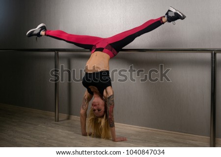 40 years fit sporty blond hair woman is doing hand stand with straddle in front of wall.