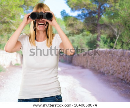 happy woman looking through binoculars at a park