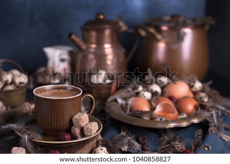 A fragrant coffee in a rustic style. Many feathers. Dark photo. Chicken and quail eggs for Easter. Metal vintage dishes. View from above