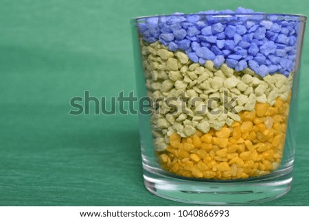 Yellow, blue and green small rocks in the Glass on the green Background