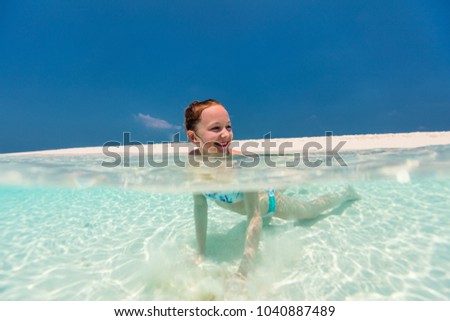 Split underwater photo of a little girl swimming in tropical ocean