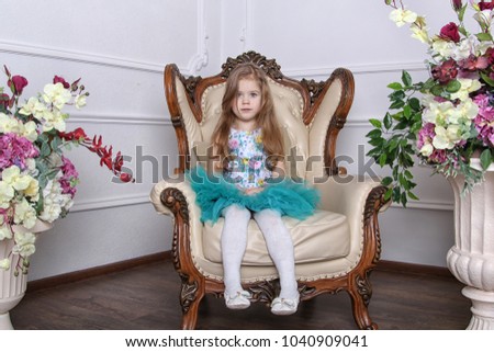 Little cute girl is sitting in a chair in a beautiful dress. 