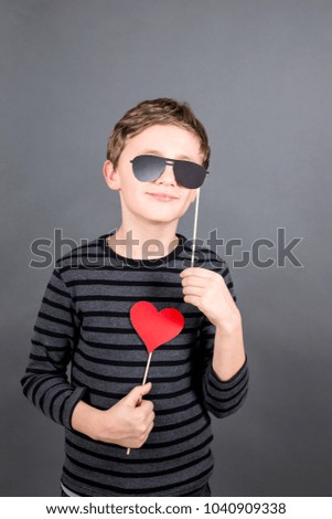 cool young blonde boy with a red heart an black sunglasses. grey background