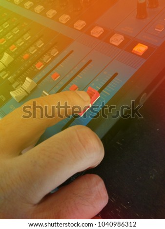 Close Up Man Hand Controlling Audio Mixer, with yellow and Red Light Flare