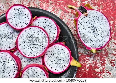 Appetizing sliced white pitahaya on the wet black plate on the shabby wooden red table. Half of a dragon fruit lies near it. Closeup top view photo. Horizontal.