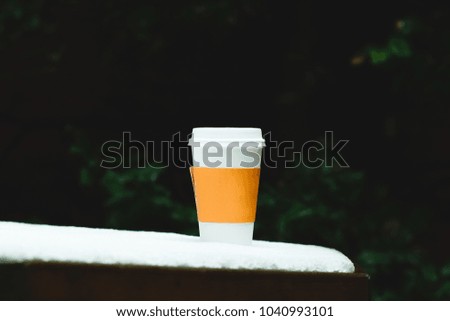 Hot coffee tea on snowy table with shallow depth to field bushes in the winter time warm comforting 