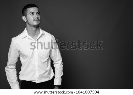 Studio shot of young multi-ethnic Asian businessman wearing white shirt against gray background in black and white