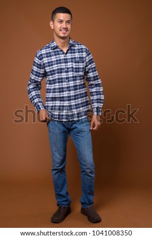 Studio shot of young multi-ethnic Asian man wearing blue checkered shirt against brown background