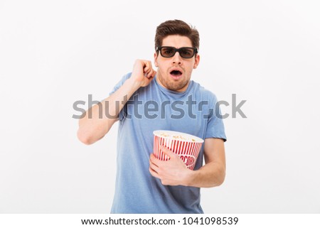 Photo of caucasian guy in casual t-shirt and 3d glasses eating popcorn and emotionally watching movie in cinema isolated over white wall
