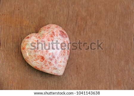 Pink heart made of natural stone rhodochrosite. A heart shaped stone lies on a brown or beige background. Love talisman, zen, spa.