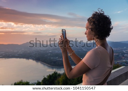 Young slim brunette woman with curly hair girl takes selfie photo pictures on observation deck view point on tropical asian Phuket island, Thailand