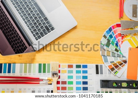 Laptop,paints,brushes and accessories on wooden table for home renovation,professional decorator drawing on a house project with work tools,teamwork,idea concept.