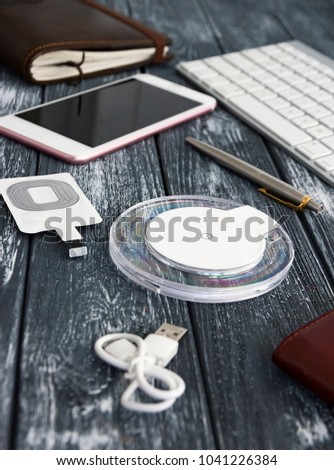 Stylish and elegant composition for business negotiations or website design. Wireless charging for the smartphone, keyboard, wallet, steel pen and glasses lie on a stylish vintage dark desk.