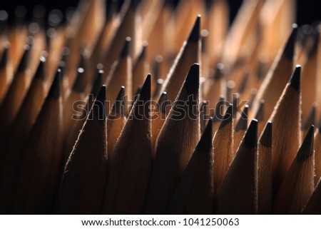 Close Up of bunch of identical sharp graphite pencils on black background with shallow depth of field. . Studio shot. Concept of uniformity. Concept of similarity.