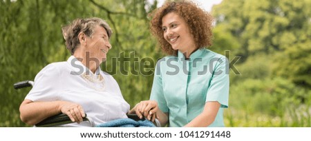 Positive picture of a smiling old woman in wheelchair and her assistant