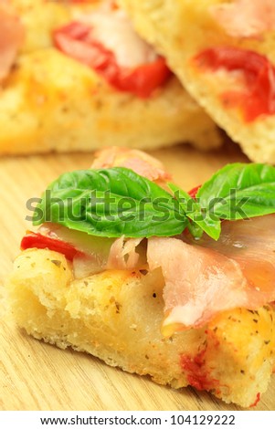 Italian focaccia bread with ham and tomatoes, topped with a leaf of fresh basil