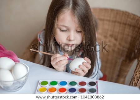 Little cheerful active child girl long hair paints an egg with pink paint on Easter. Spring traditions