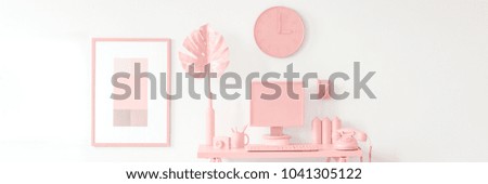 Phone and monstera leaf on desk against white wall with clock and poster in peach workspace interior